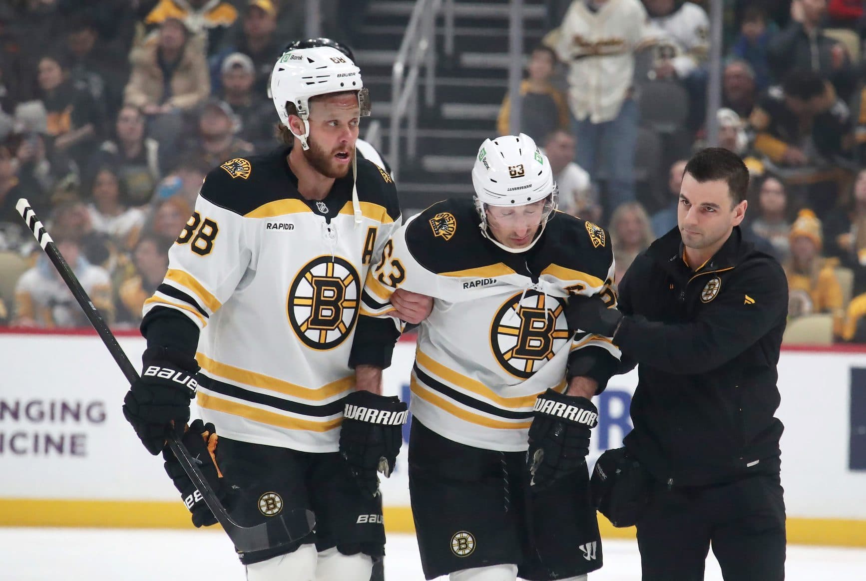 Boston Bruins left wing Brad Marchand (63) is helped from the ice by right wing David Pastrnak (88) and a team trainer after suffering an apparent injury against the Pittsburgh Penguins during the first period at PPG Paints Arena.